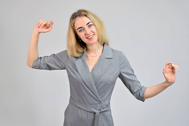 Portrait of a pretty cute smiling young blonde business woman with minimal makeup in a gray suit on a white background. Model Standing directly in front of the camera in various poses. - Fotó, kép