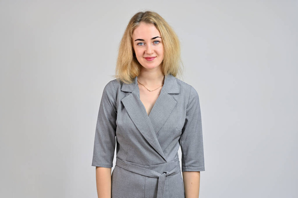 Portrait of a pretty cute smiling young blonde business woman with minimal makeup in a gray suit on a white background. Model Standing directly in front of the camera in various poses. - Fotografie, Obrázek