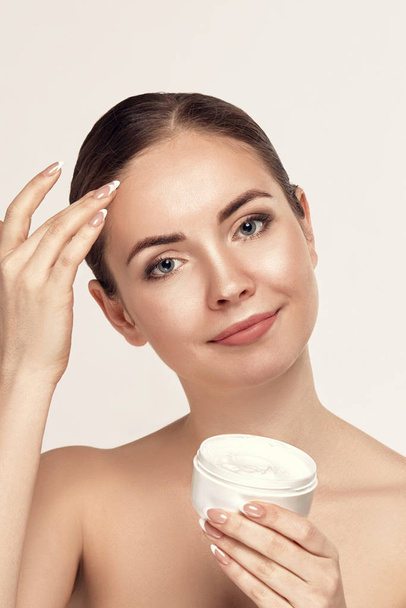 Beauty Woman Concept. Skin care. Portrait of female model  holding and applying cosmetic moisturizing cream and touch own face. Skin Protection. Cosmetology. Spa. - Foto, imagen