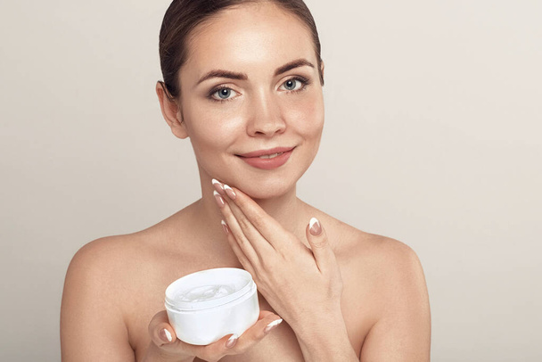 Beauty Face of Woman Concept. Skin care. Portrait of female model  holding and applying cosmetic moisturizing cream and touch own face. Skin Protection. Cosmetology. Spa - Foto, Bild