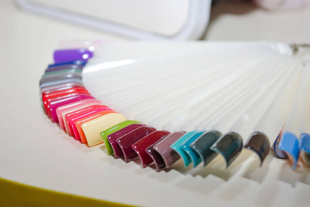 Paleta de diseño de uñas de diferentes colores con gel esmalte sobre puntas blancas y fondo. Probadores de plástico para esmalte de uñas
 - Foto, Imagen