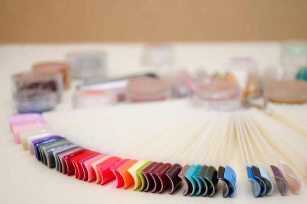 Палітра дизайну нігтів різних кольорів з гелевим лаком на білих кінчиках і фоні, банки з блискітками і декором
 - Фото, зображення