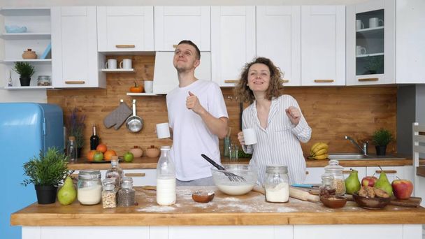 Young Couple With Coffee Cups Dancing Together In Kitchen While Cooking Breakfast. - Φωτογραφία, εικόνα