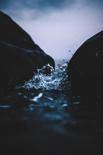 Víz üti sziklák és kis cseppek fröccsen a kamerába - Fotó, kép