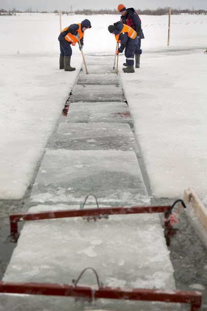 Arbeiter treiben Eisblöcke entlang eines Kanals, der von einem zugefrorenen See geschnitten wurde - Foto, Bild