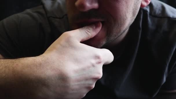 Zenuwachtige man in een grijs T-shirt bijt zijn nagel met zijn tanden, close-up. Hoofdportret van een man met een nerveuze uitdrukking die op zijn nagels bijt. Een man eet nagels, close-up, menselijke problemen en slechte gewoonten. - Video