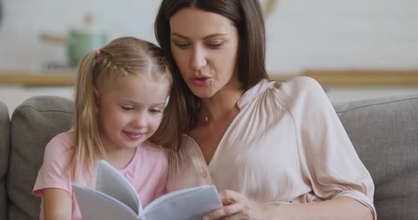 Focused young mother reading interesting story to daughter. - Záběry, video