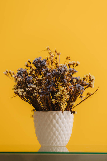 Fleurs sauvages séchées. Beaucoup de petites fleurs bleues et jaunes dans un vase blanc. Bouquet sur fond jaune
. - Photo, image