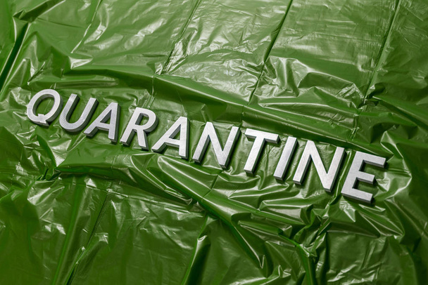 the word quarantine laid with silver letters on green crumpled plastic film background in diagonal perspective - Photo, Image
