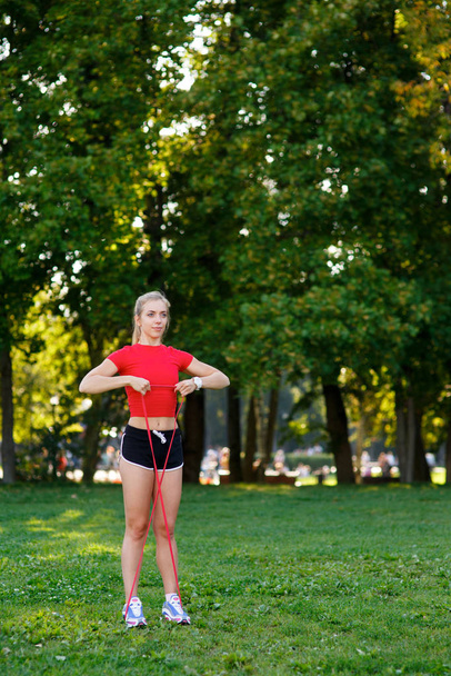 Young woman is training with rubber bands outdoors. Healthy active lifestyle concept. girl doing fitness in the park on the nature - Valokuva, kuva