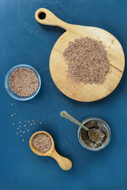 Flaxseeds in a wooden spoon with flax paste on a dark background. Vertical orientation, top view. - Photo, Image