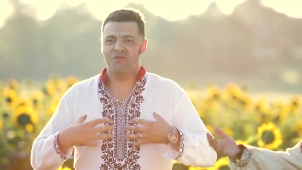 Група молодих щасливих людей в національному українському одязі співає і танцює на соняшникових полях влітку
. - Кадри, відео