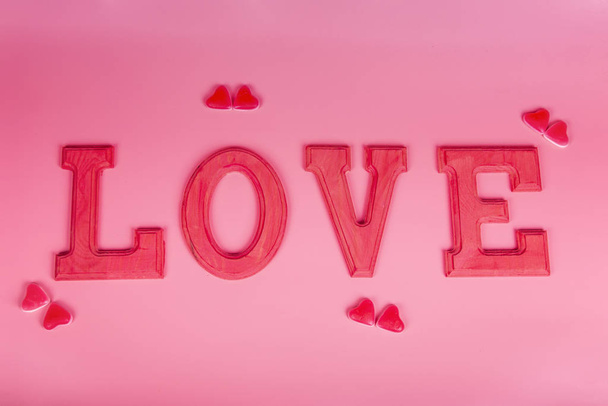 Word love in fuxia wooden letters with jelly beans hearts on pink background. Selective focus. Valentine, love concept. - Фото, зображення