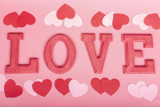 Word liefde in fuxia houten letters met papieren hartjes op roze achtergrond. Selectieve focus. Valentijn, liefde concept. - Foto, afbeelding