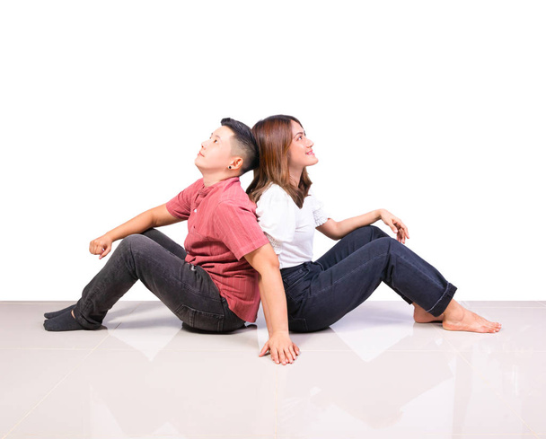 Dos chicas jóvenes sonrientes y amigos tomboy felicidad sentados espalda con espalda cogida de la mano en el suelo de baldosas en casa con fondo blanco
 - Foto, Imagen