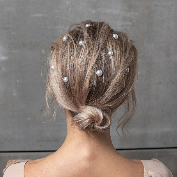Девушка с жемчугом в волосах против серой стены, вид сзади крупным планом. мода прическа
 - Фото, изображение