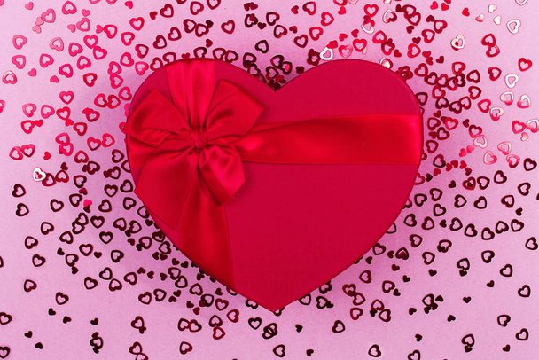 Red gift box heart shape with red ribbon on a pink sequinbackground, gift concept Valentine day, top wiev, c - Photo, Image