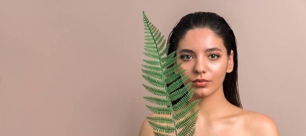 portrait of a tender woman with green eyes looking out of palm leaf - Foto, Imagem