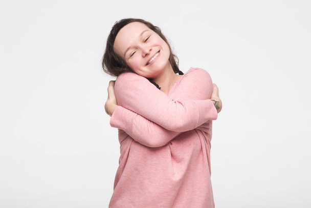 Pretty caucasian teenager in pink clothes hugging herself being proud feeling comfortable. - Photo, Image