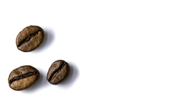 Hintergrund aus drei Kaffeebohnen, gerösteten Kaffeebohnen mit selektivem Fokus auf weißem Hintergrund, Platz für Text. - Foto, Bild