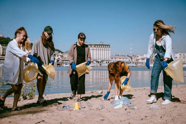 Group of activists friends collecting plastic waste on the beach. Environmental conservation. - 写真・画像