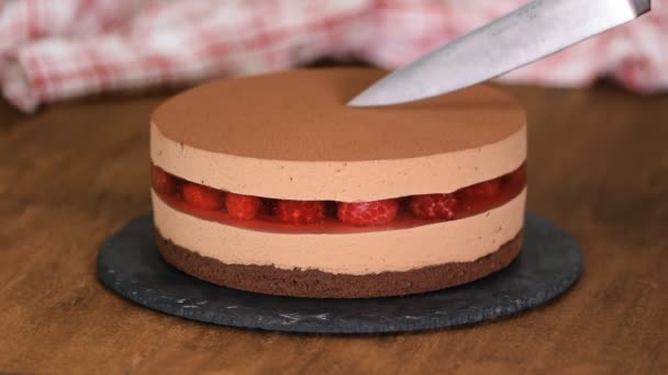Womans hands cut the delicious chocolate mousse cake with raspberries jelly. - Video, Çekim