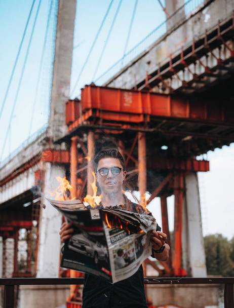 Guy reads a burning newspaper, in the background a bridge - Фото, изображение