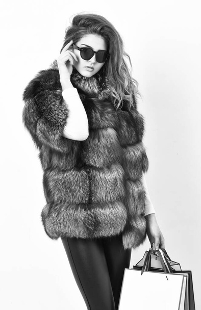 Woman shopping luxury boutique. Lady hold shopping bags. Discount and sale. Buy with discount on black friday. Shopping or birthday gift. Girl wear sunglasses and furry coat shopping white background - Photo, Image