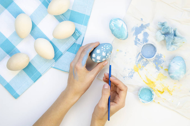 Vrouw versiert kunstmatige kippeneieren voor Pasen. Schilderen in blauwe tinten met een borstel. Top view handgemaakt Pasen concept op een witte tafel - Foto, afbeelding