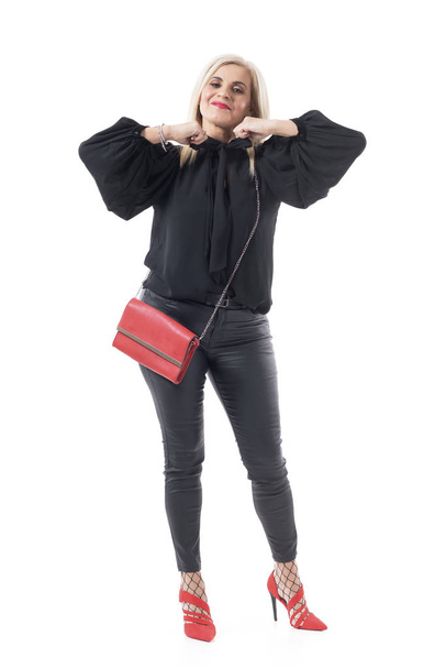 Tyylikäs moderni elinvoimainen keski-ikäinen nainen mustassa pullistuneessa puserossa ja nahkahousuissa pukeutumassa. Koko kehon pituus eristetty valkoisella pohjalla
.  - Valokuva, kuva