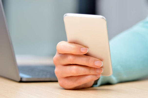 Close up of a woman hand using a silver smart phone on a desk at home - Photo, image