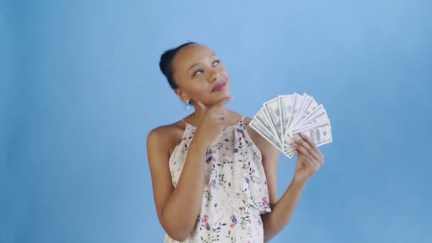 Thoughtful successful african american woman with money on blue background. White dress with flowers - Video, Çekim