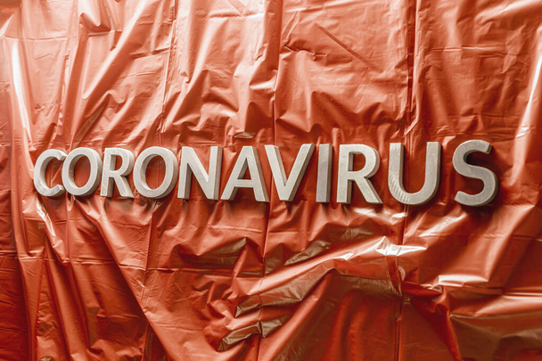 Coronavirus kelimesi buruşuk mavi plastik paltoya gümüş harflerle işlenmiş. - Fotoğraf, Görsel