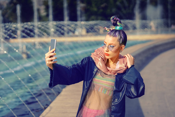Cool hipster funky jeune fille influenceuse de mode avec des cheveux fous et un style avant-gardiste prendre selfie dans la rue - femme partage du contenu à la mode sur la plate-forme de streaming et plate-forme de médias sociaux
 - Photo, image