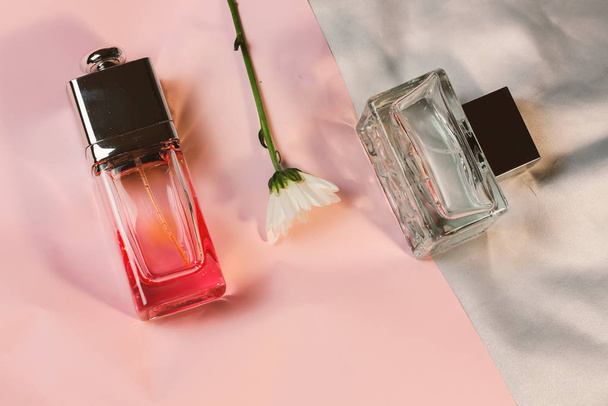 Transparent glass fashion trendy bottles of perfume toilet water fragrances on a pink silver background with delicate white gentle daisies chamomile, trendy modern flat lay with heavy shadows - Foto, Imagem