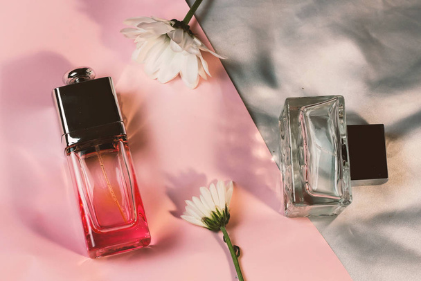 Transparent glass fashion trendy bottles of perfume toilet water fragrances on a pink silver background with delicate white gentle daisies chamomile, trendy modern flat lay with heavy shadows - Foto, imagen