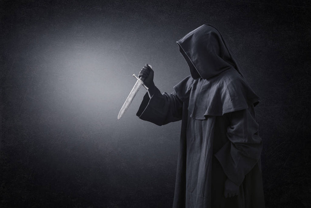 Hooded man with ancient knife in the dark - Foto, Imagen