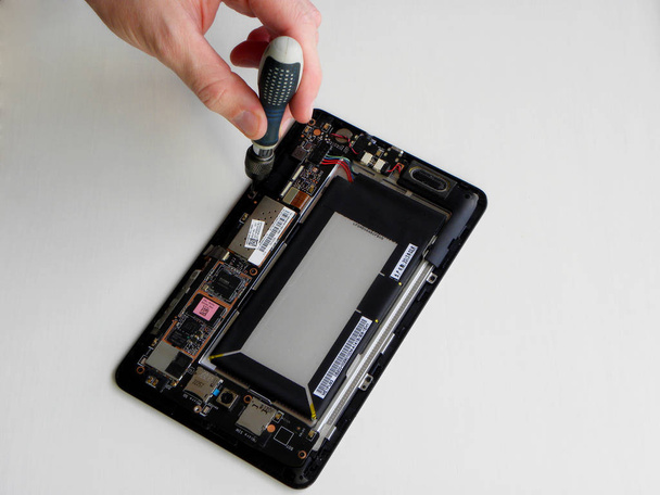          Concept of  tablet repair .  The technician holds a screwdriver in his hand over the damaged tablet, fixing and upgrading the technology.                                    - Foto, imagen