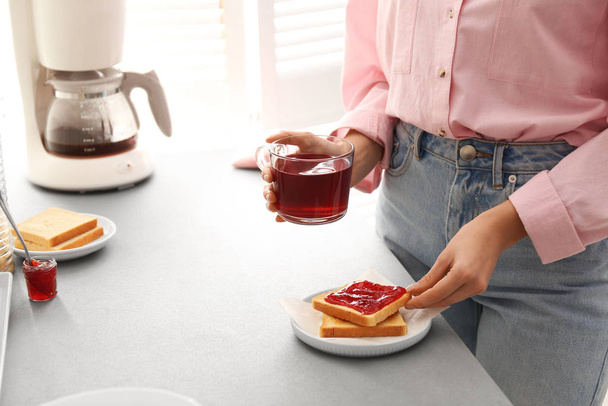 Kobieta je smaczne śniadanie z tostami i malinową herbatą w domu, zbliżenie. Poranna rutyna - Zdjęcie, obraz