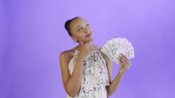 Thoughtful successful african american woman with money on purple background. White dress with flowers - Video