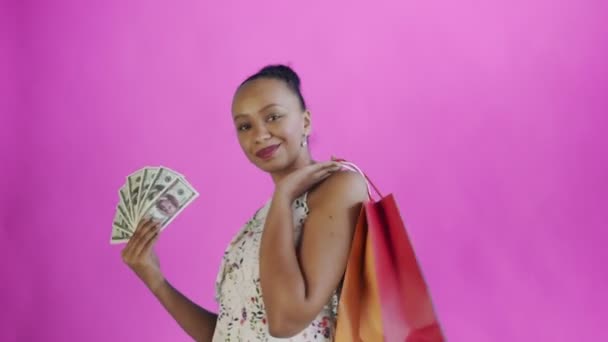 African american woman with money card and shopping bags. Pink backgound. White dress with flowers - Filmmaterial, Video