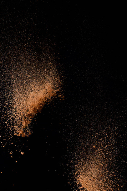 Cocoa powder explosion in motion on black background. Chocolate dust.  - Фото, изображение