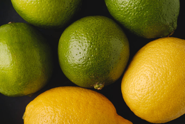 Citrónové a citrónové kyselé plody v černém talíři, pohled shora, vitamíny a zdravé jídlo, zblízka makro textura - Fotografie, Obrázek