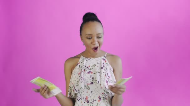 Attractive Afro american woman is counting money against a pink background. White dress with flowers - Séquence, vidéo