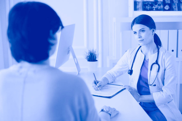 Az orvos és a beteg egy kórházi rendelőben beszélik meg az orvosi problémákat. Betegnyomtatványt kitöltő doki - Fotó, kép