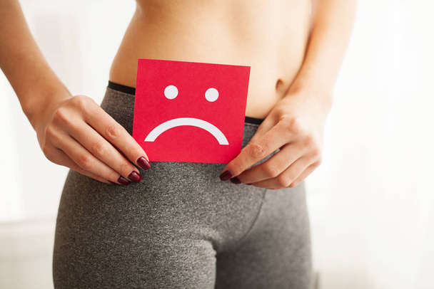 Frauengesundheit. weiblicher Körper hält traurige Smiley-Karte in der Nähe des Magens. - Foto, Bild