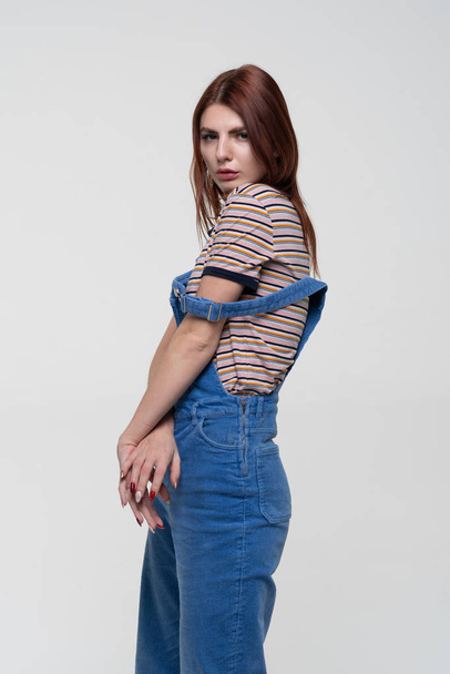 young pretty woman posing in studio, standing in blue overalls - Zdjęcie, obraz