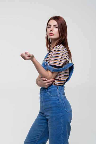 young pretty woman posing in studio, standing in blue overalls - Фото, изображение