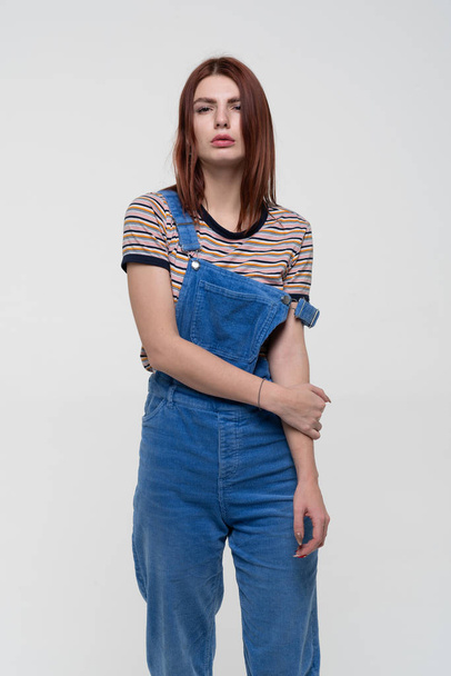 young pretty woman posing in studio, standing in blue overalls - Photo, Image