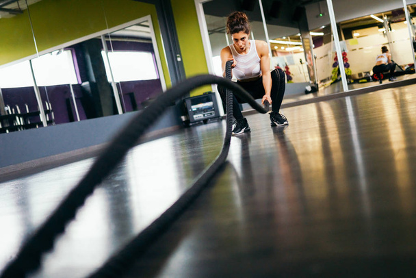 Young and athletic woman using training ropes in a gym. - Photo, Image